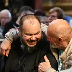 Dwóch mężczyzn w kościele, jeden z nich śmieje się serdecznie, drugi obejmuje go ramieniem. W ich relacji widać radość i wsparcie, jakby mówili: ora et labora.