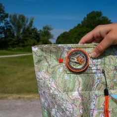 Ręka trzyma mapę i kompas, gotowa do podróży. Obieżyświat wyrusza na szlak, by odkrywać nowe miejsca.