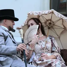 Elegancka arystokracja w lalce, mężczyzna w cylindrze i fraku, kobieta z wachlarzem i parasolką.