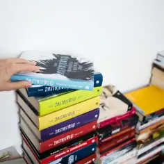 Dłoń sięga po książkę "Wspomnienia z martwego domu" Dostojewskiego, leżącą na stosie kolorowych powieści.