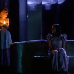 Dwie kobiety na scenie, jedna z lampą, druga na kanapie. Scena jak z teatrum mundi, pełna mroku i tajemnicy.