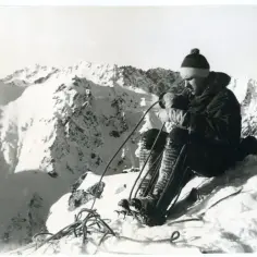 Alpinista w zimowym krajobrazie, przygotowujący sprzęt. Jego postawa emanuje spokojem i determinacją, świadcząc o heroizmie w obliczu surowej natury.