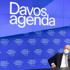 Klaus Schwab, globalny kosmopolita, w masce na tle logo World Economic Forum w Davos.
