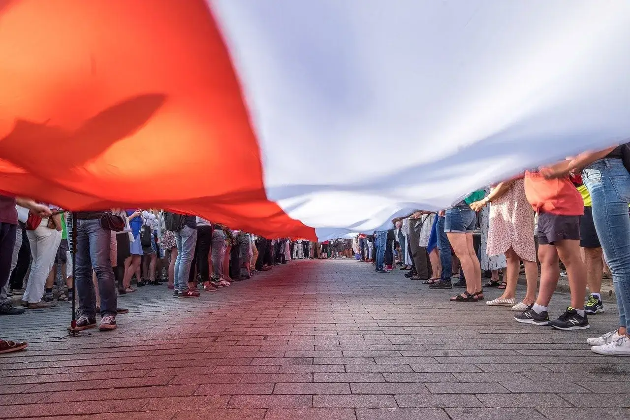 Ludzie trzymają ogromną biało-czerwoną flagę, tworząc żywy obraz patriotyzmu. Definicja patriotyzmu w akcji.
